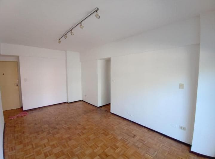 Living vacío con piso de parquet y puerta de entrada.