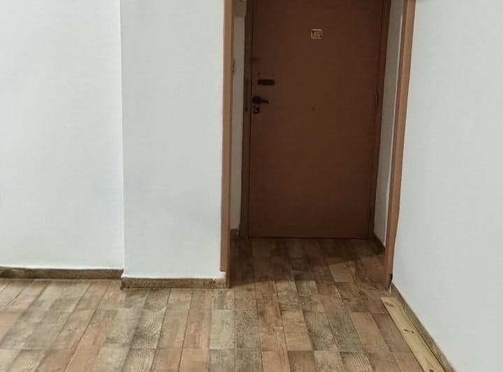 Pasillo de entrada con puerta, piso símil madera y paredes blancas.