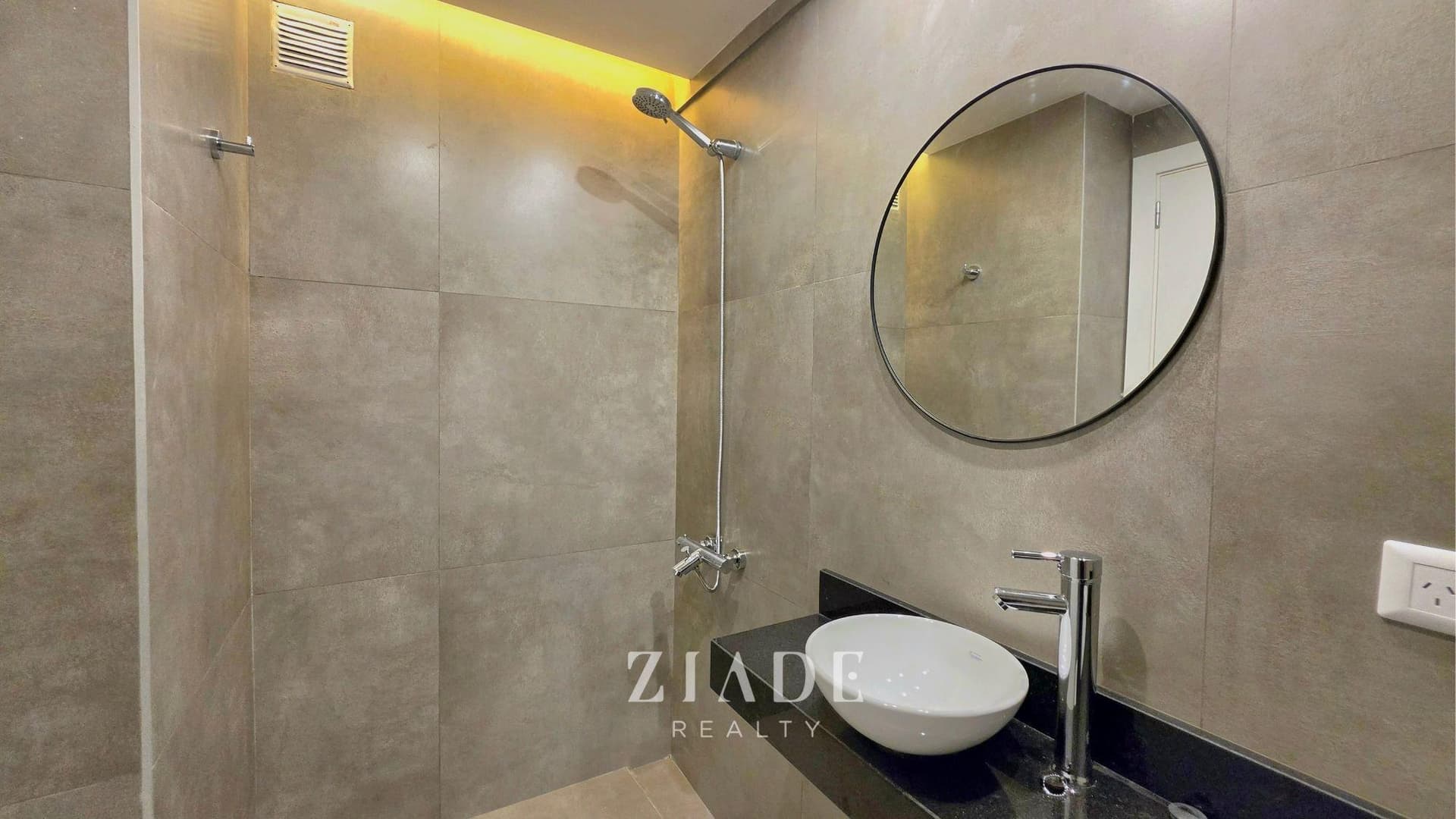 Baño moderno con ducha empotrada, vanitory con bacha redonda y espejo circular.