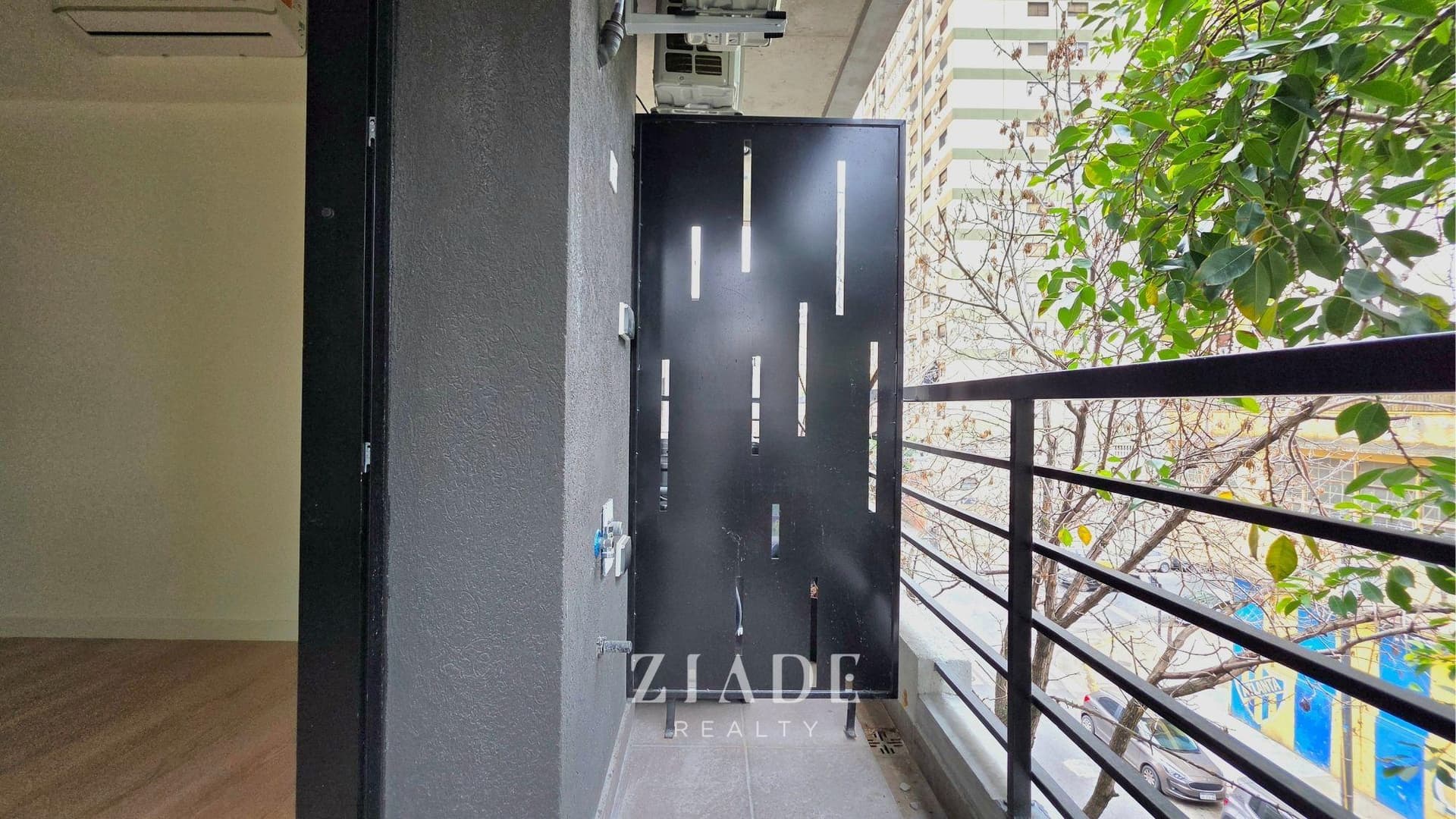 Balcón con rejas de seguridad y vista lateral hacia la calle con árboles.