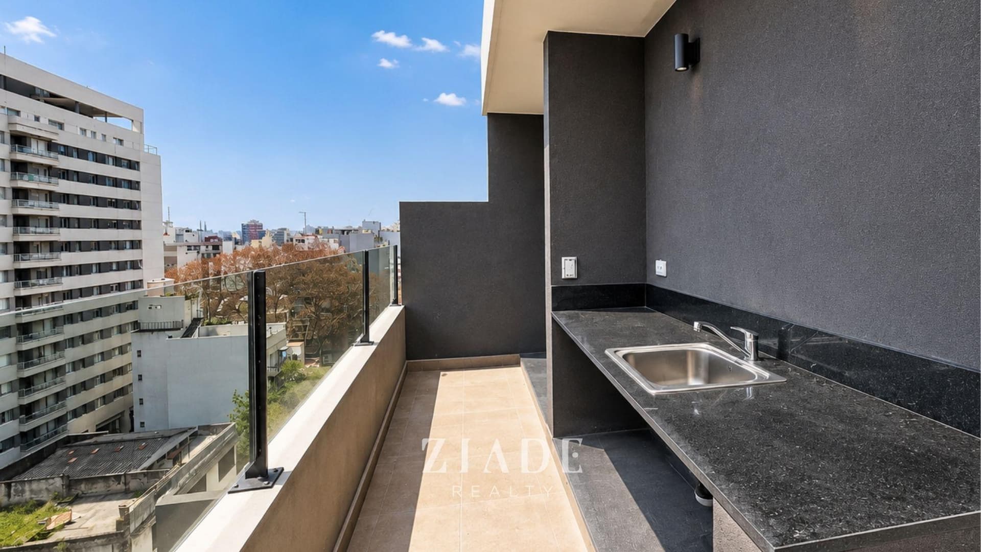Terraza común con mesada, bacha exterior y baranda de vidrio con vistas.