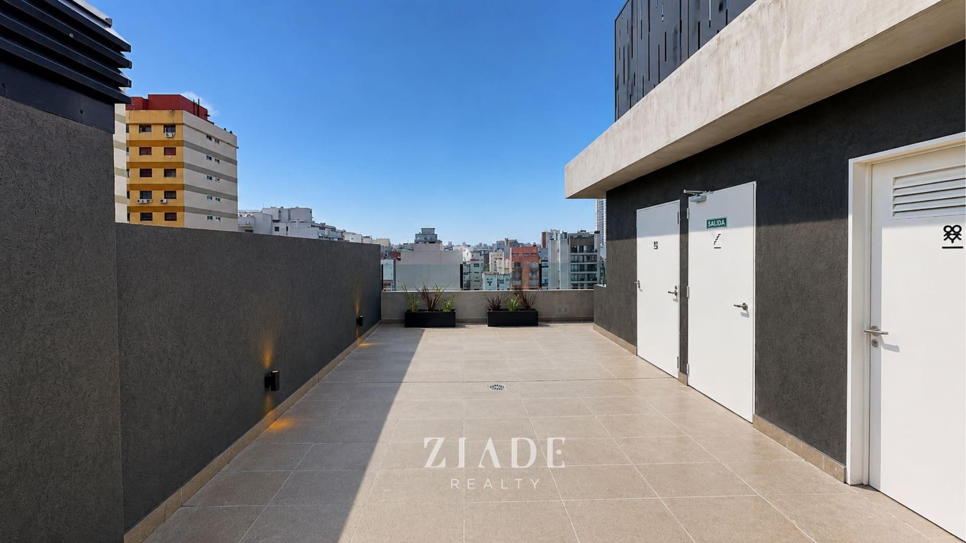 Amplia terraza común con puertas de acceso y vista a los edificios vecinos.