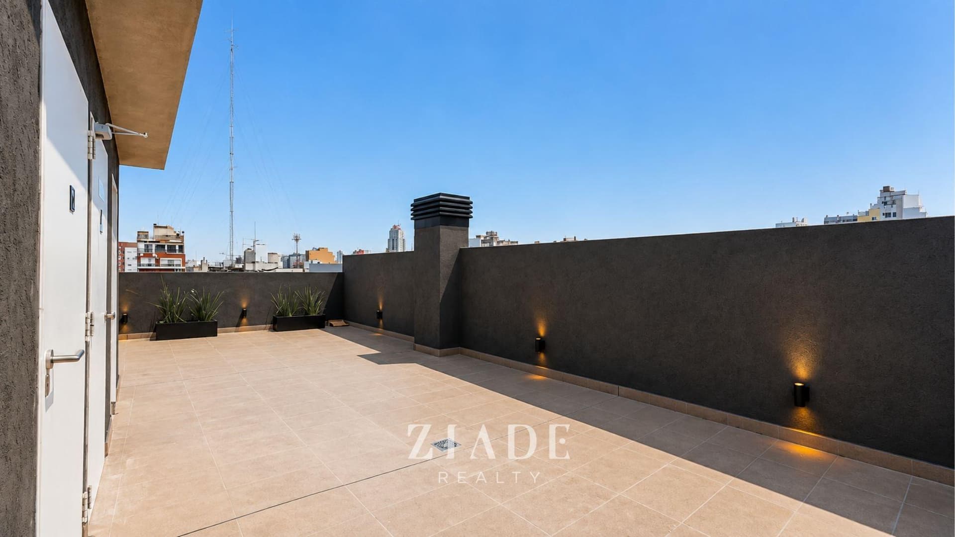 Terraza común con iluminación exterior, paredes oscuras y espacio abierto.