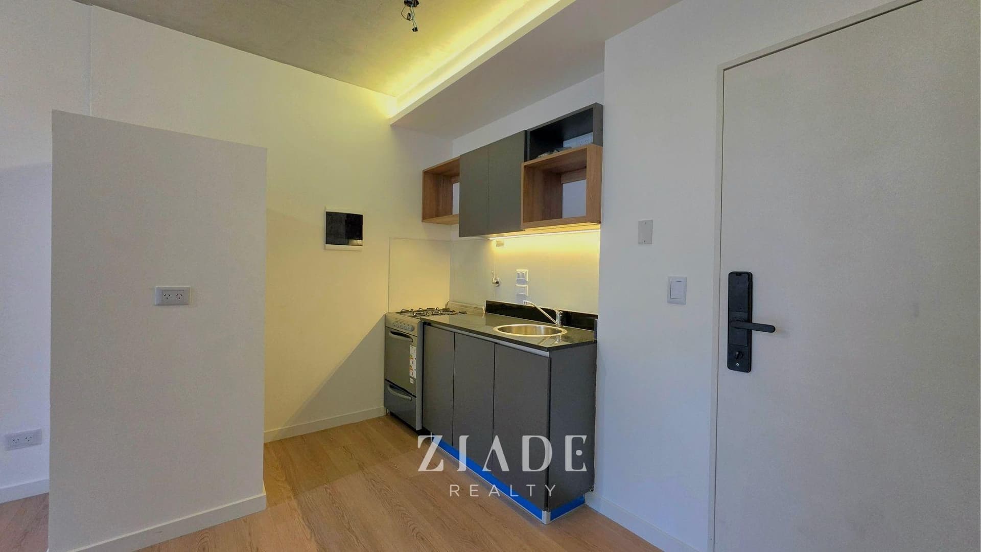 Cocina integrada con anafe, bacha, alacenas en gris y madera, mesada oscura.