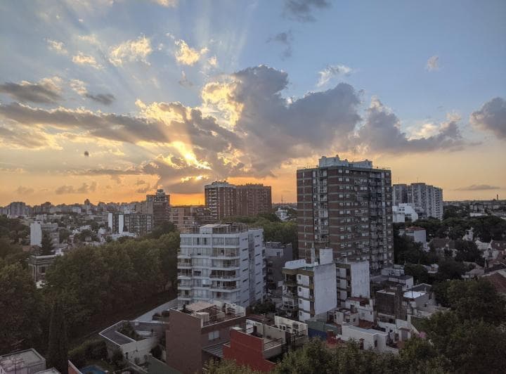 Vista panorámica de la ciudad al atardecer con nubes y sol.