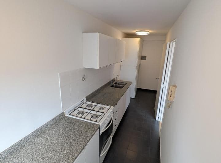 Cocina con muebles blancos, heladera, mesada y anafe.