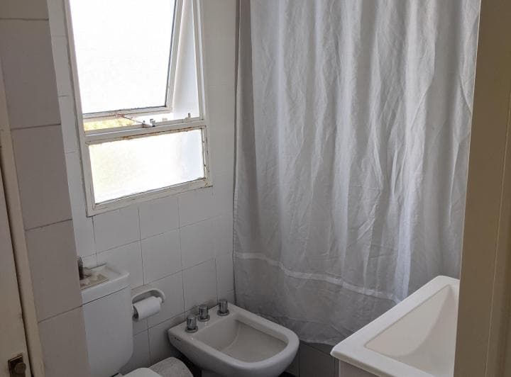 Baño con inodoro, bidet y bañera con cortina blanca.