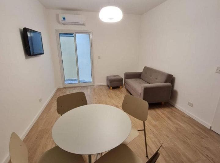 Living con sofá, televisor, mesa redonda con sillas y aire acondicionado, con salida al patio.