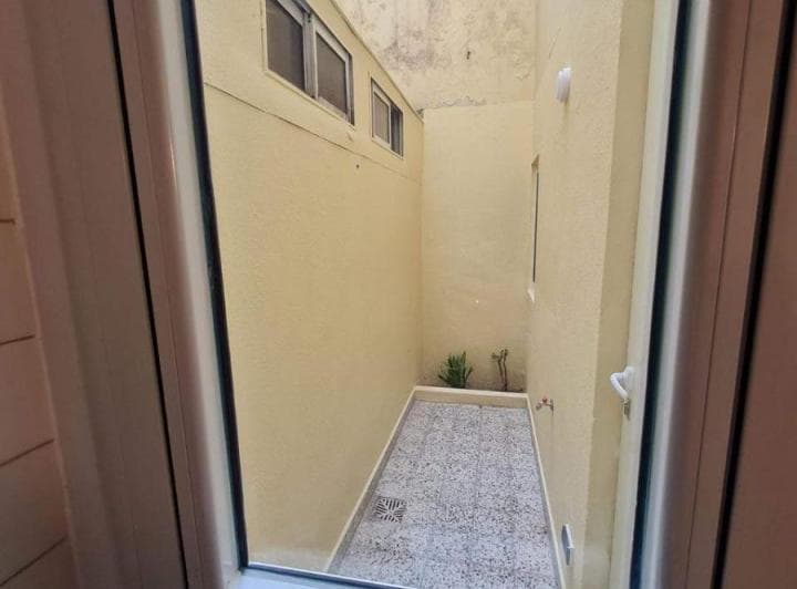 Patio exterior pequeño con paredes altas, piso de baldosas y ventanas en altura.