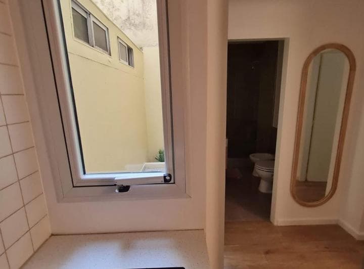 Pasillo con ventana al patio, un espejo de cuerpo entero y se ve el baño.