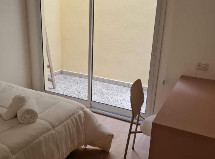 Dormitorio con cama vestida de blanco, silla y salida a un patio.
