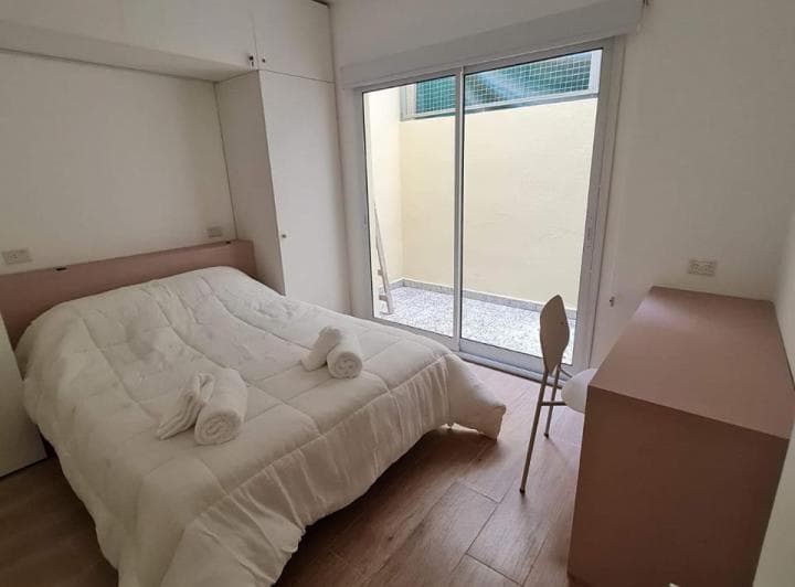 Dormitorio con cama blanca, armario y puerta ventana con salida al patio.