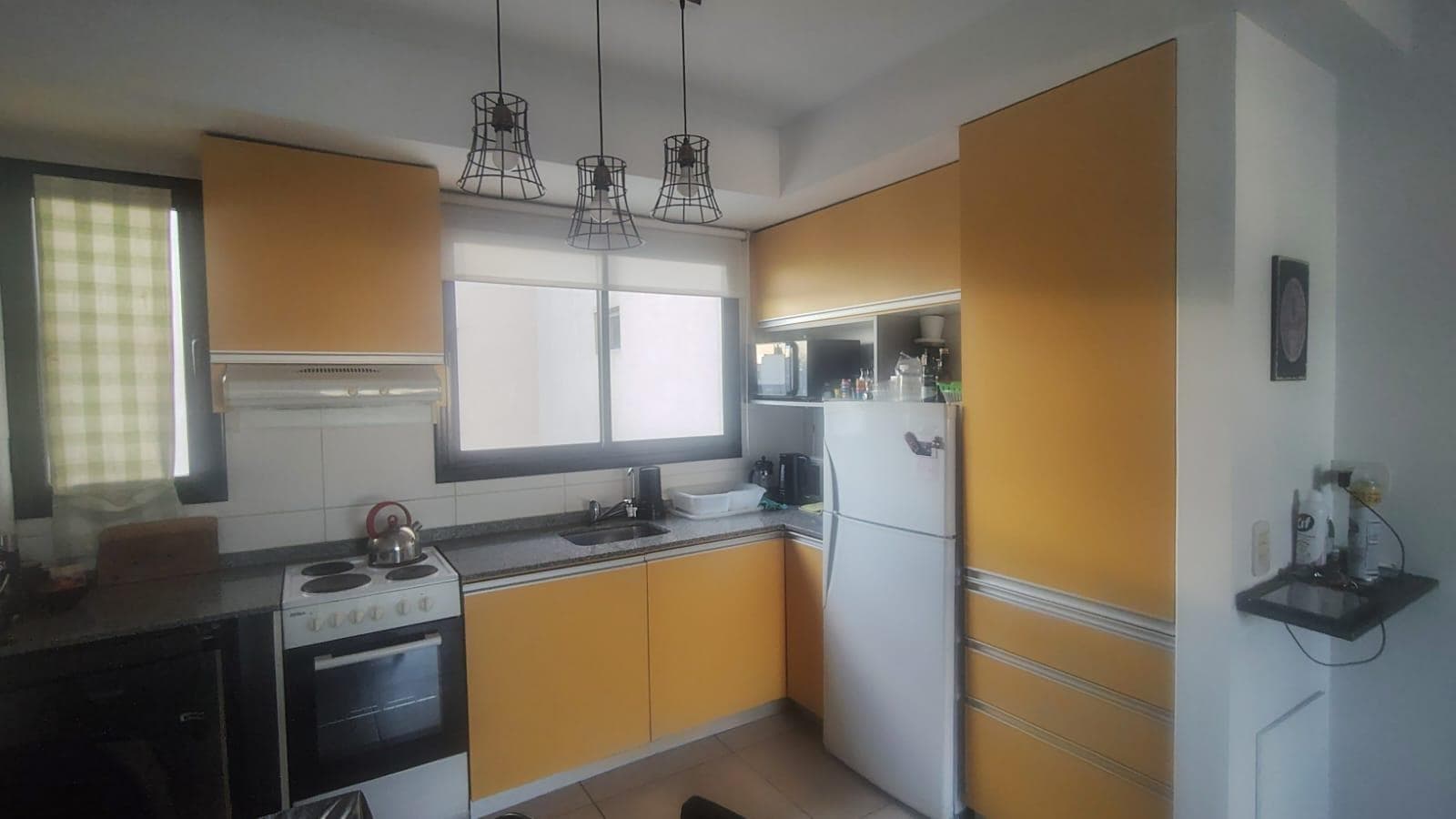 Cocina con muebles color amarillo, bacha, anafe y heladera.