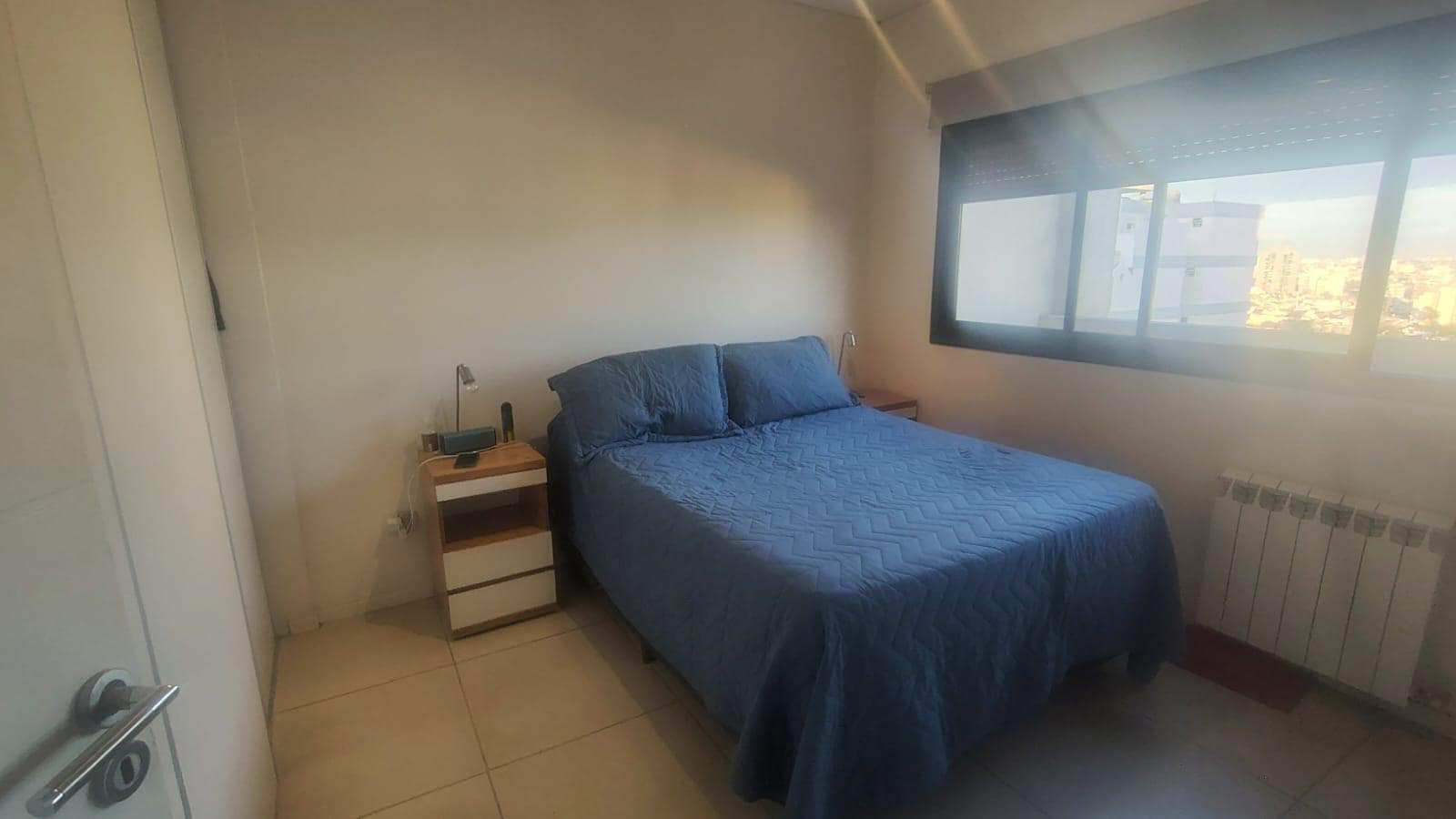 Dormitorio con cama doble, radiador y ventana con vista exterior.