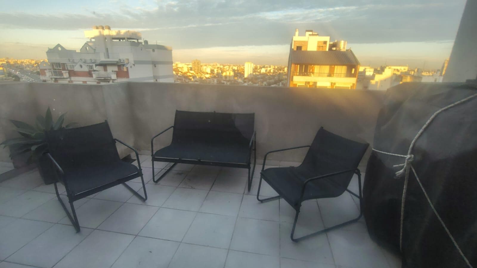 Terraza con sillas y parrilla cubierta, con vista a la ciudad.