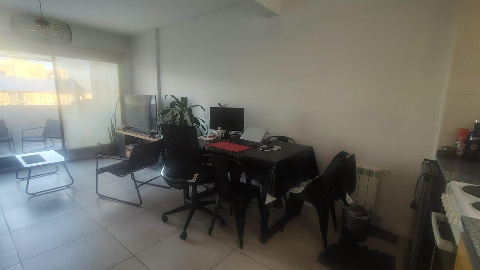 Living-comedor con mesa de trabajo, TV y salida a balcón.