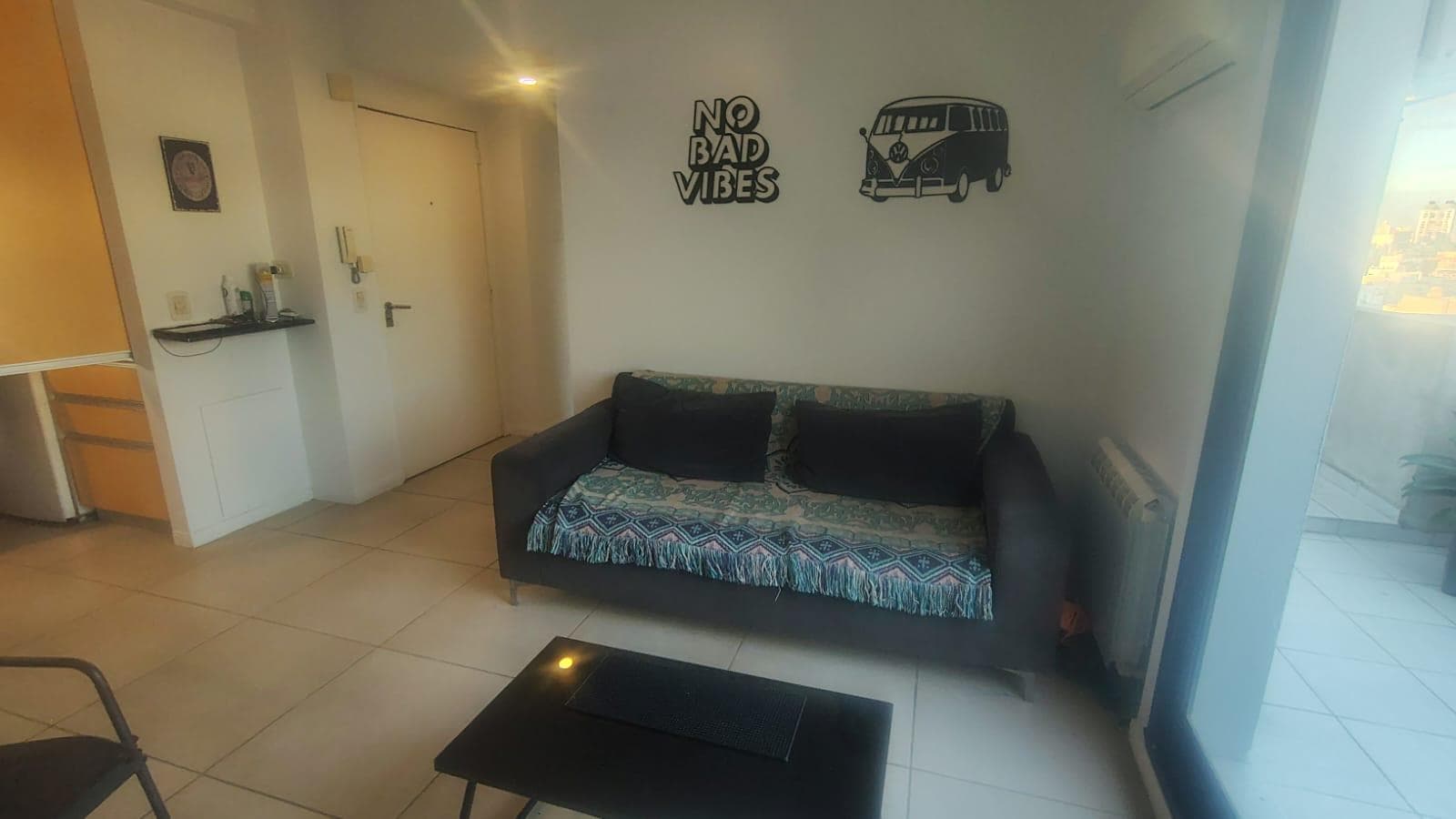Living con sillón, mesa ratona y puerta de entrada al departamento.