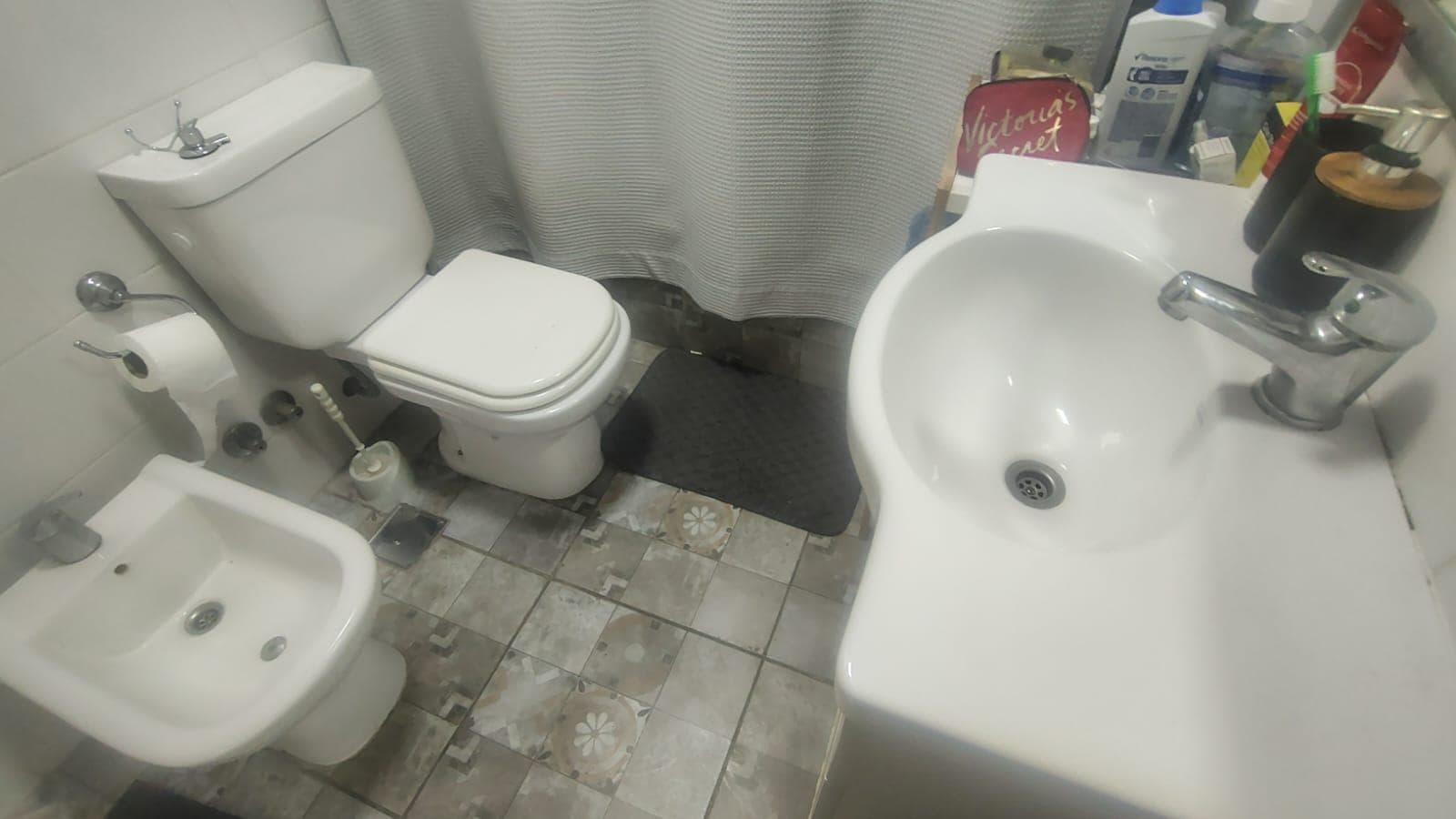 Baño con inodoro, bidet, lavatorio y cortina de ducha.