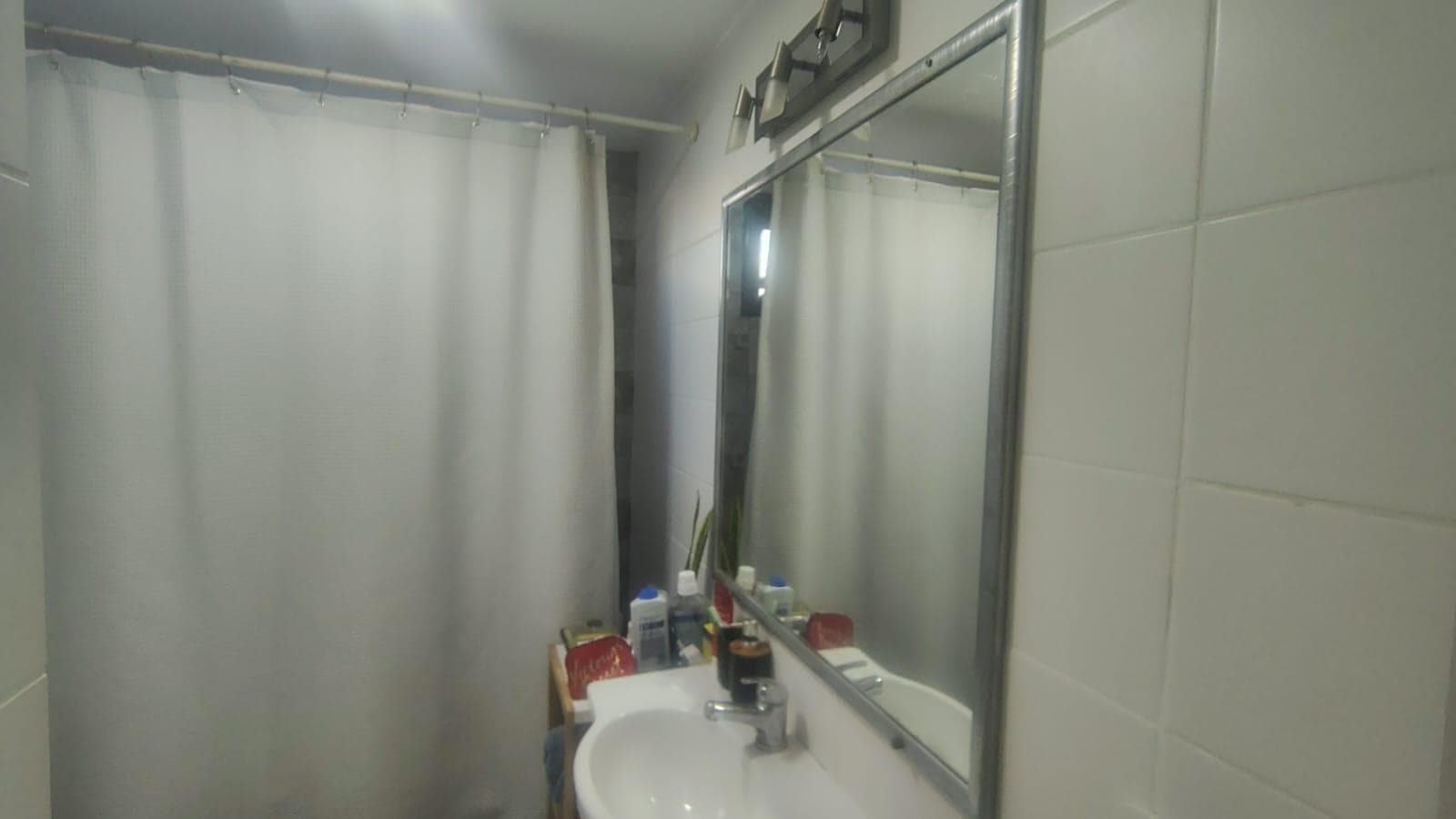 Baño con lavatorio, espejo y cortina de ducha.