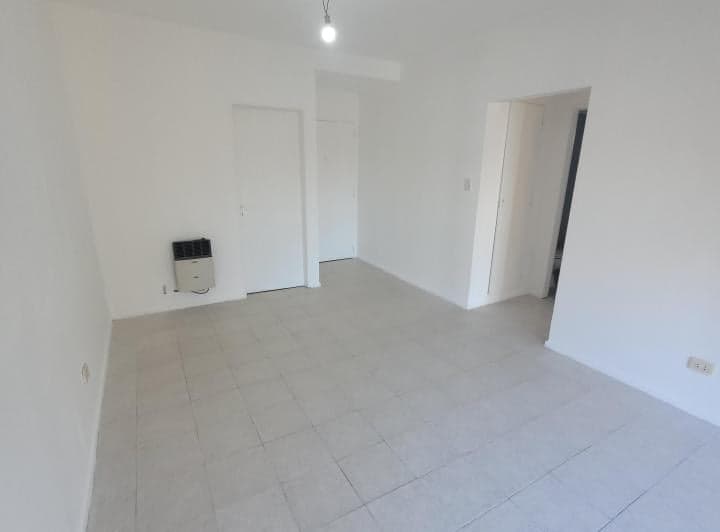 Living vacío con piso de baldosas claras, estufa y puertas.