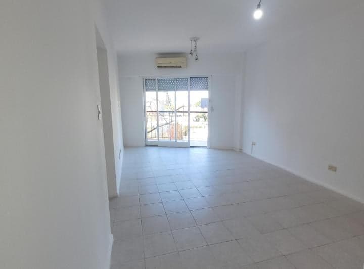 Living vacío con piso de baldosas, ventana grande y aire acondicionado.