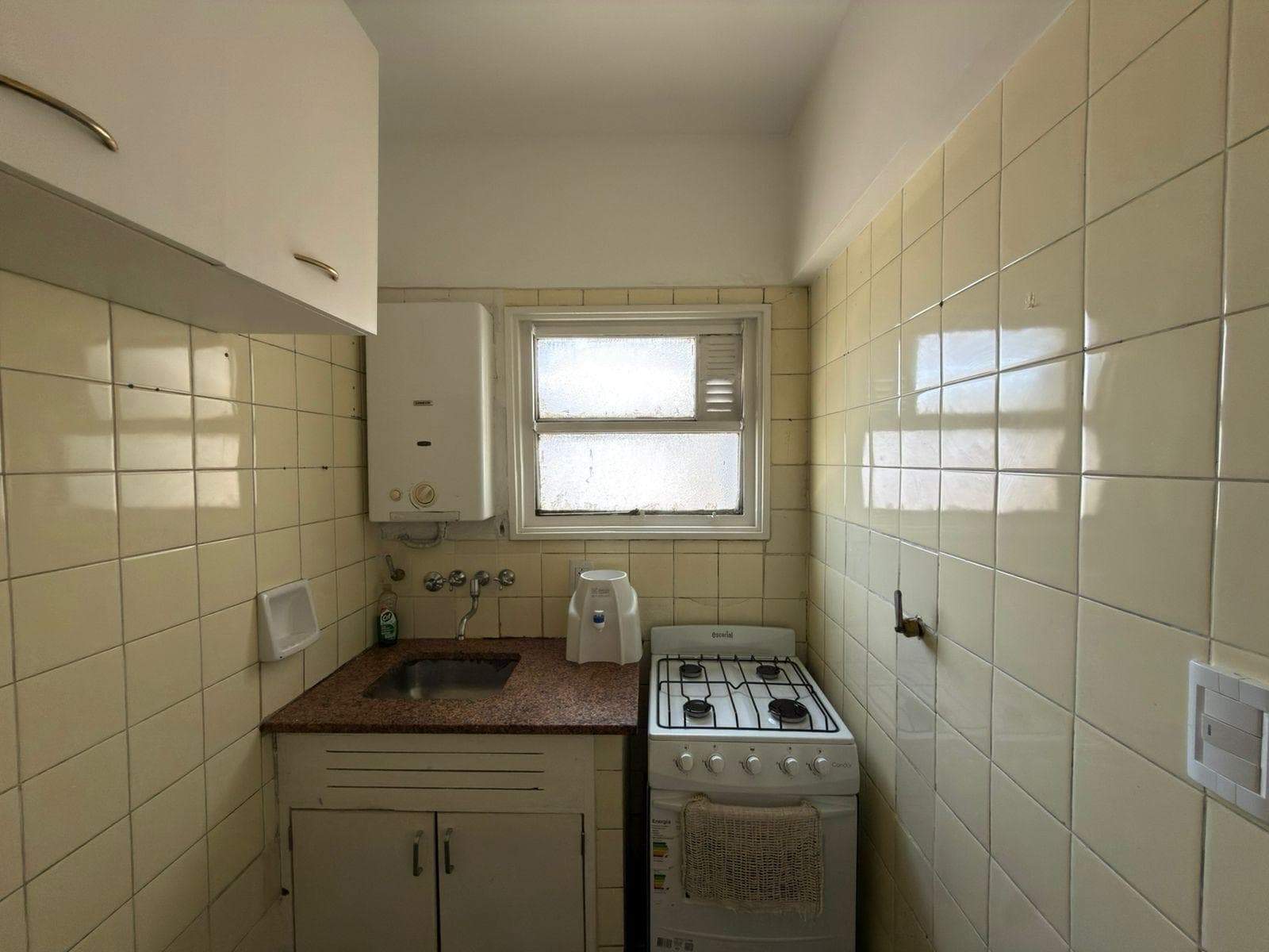 Cocina con anafe, bacha y alacena, paredes de azulejos claros.