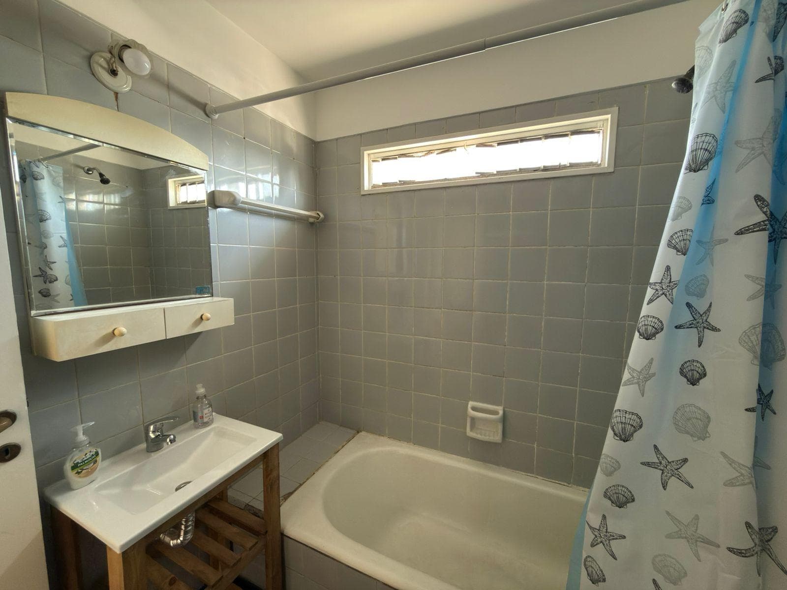 Baño con bañera, lavatorio de madera y azulejos grises.
