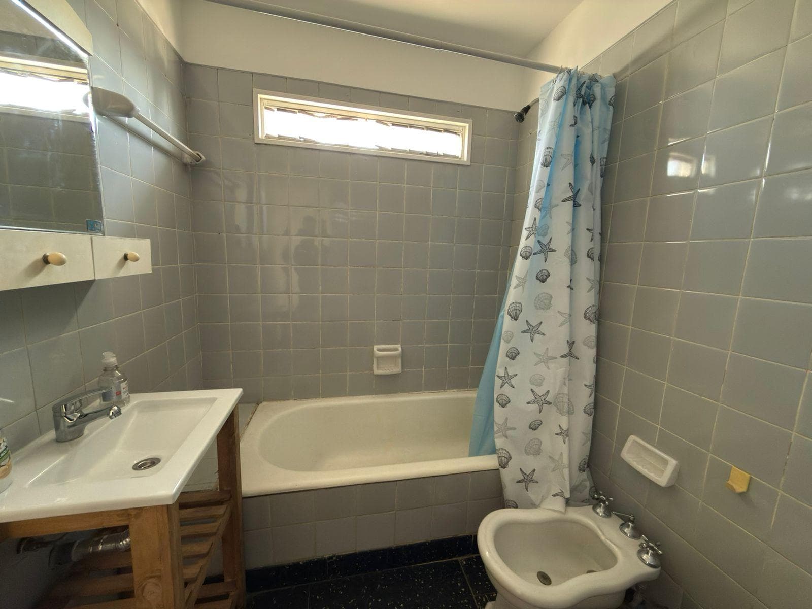 Baño completo con bañera, bidet y lavatorio, azulejos grises.