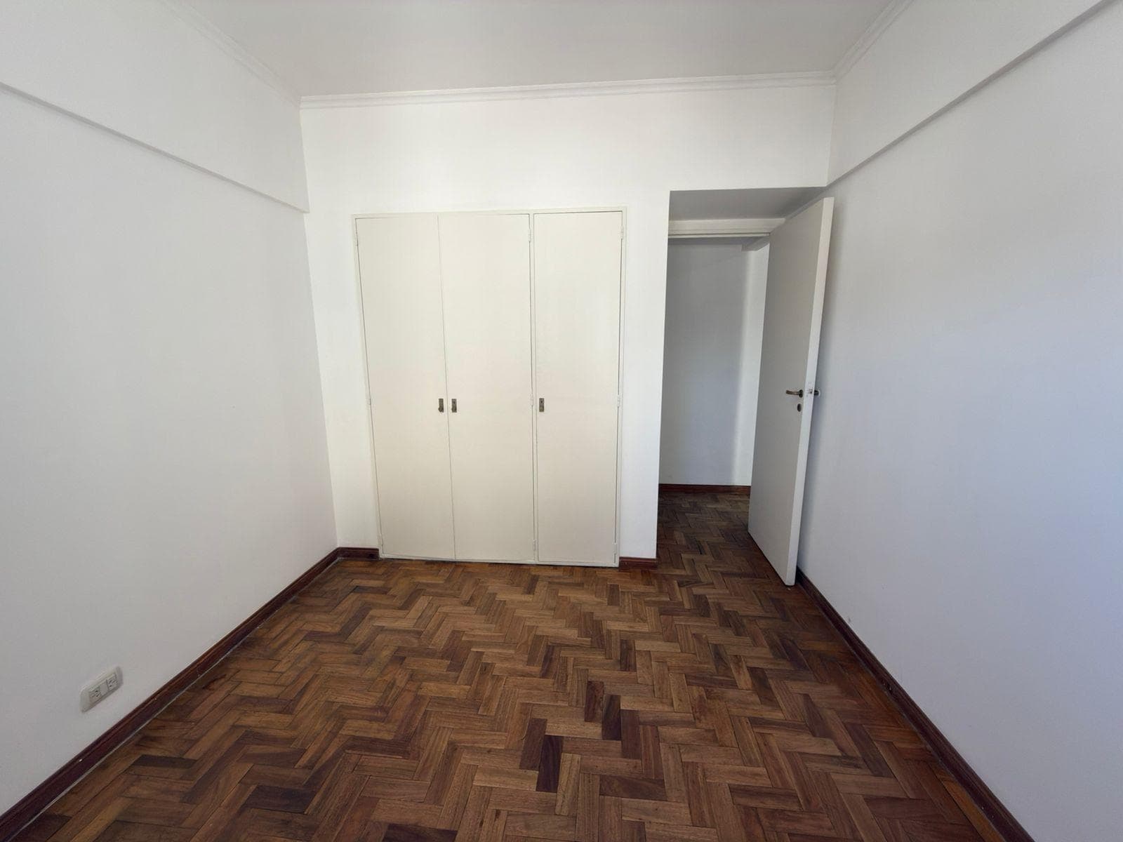 Dormitorio vacío con placard blanco y piso de parquet.