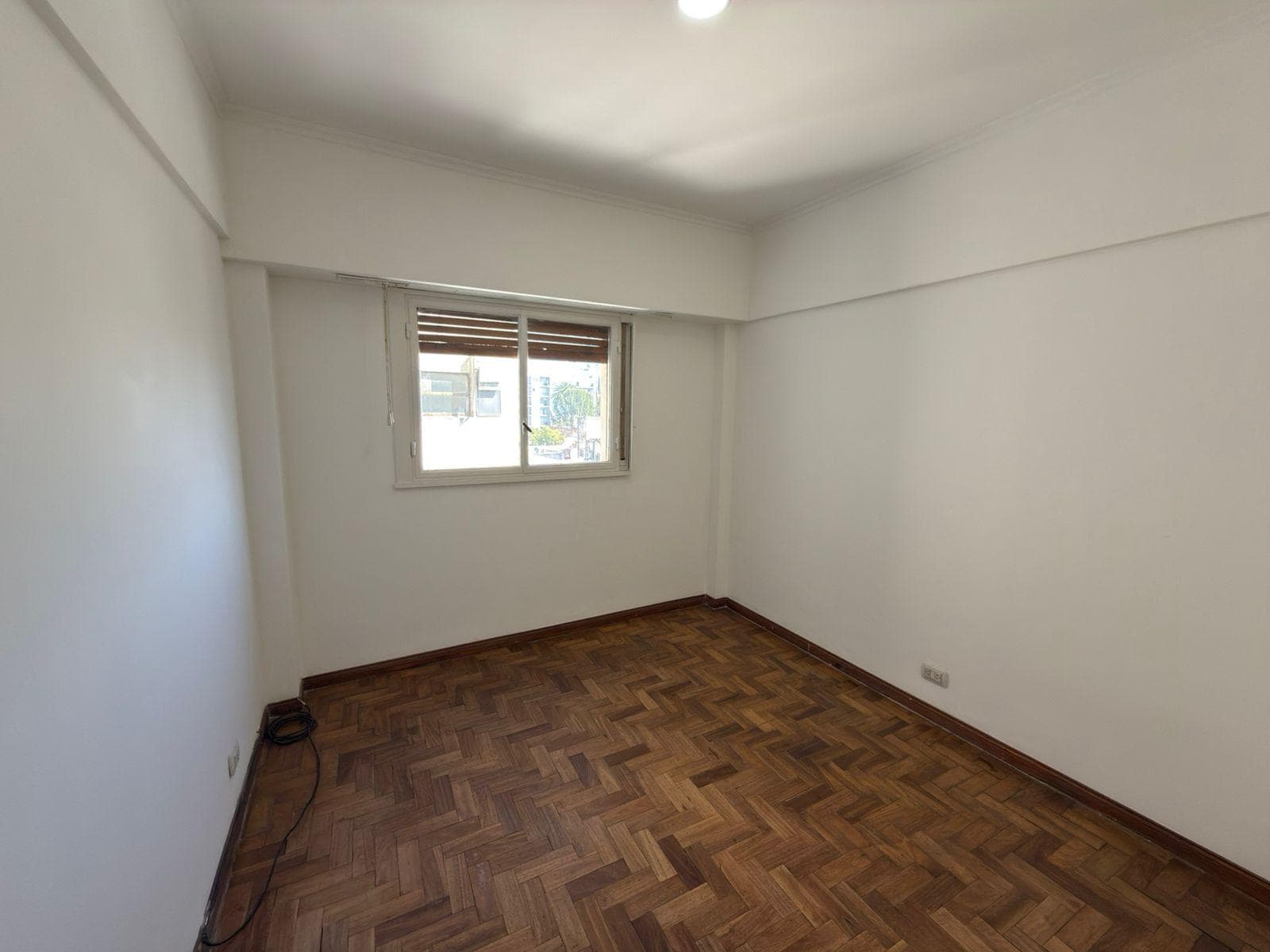 Dormitorio vacío con piso de parquet y ventana con persiana.