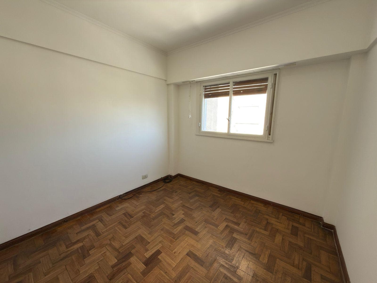 Dormitorio vacío con piso de parquet, paredes blancas y ventana.