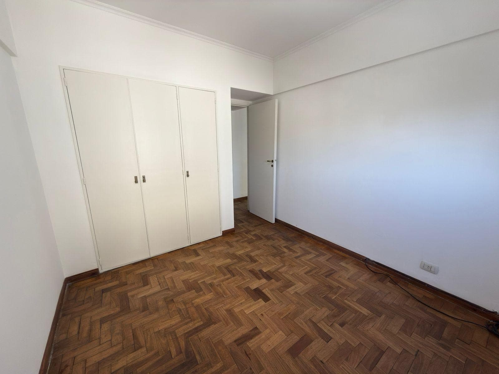 Dormitorio vacío con placard blanco y piso de parquet.