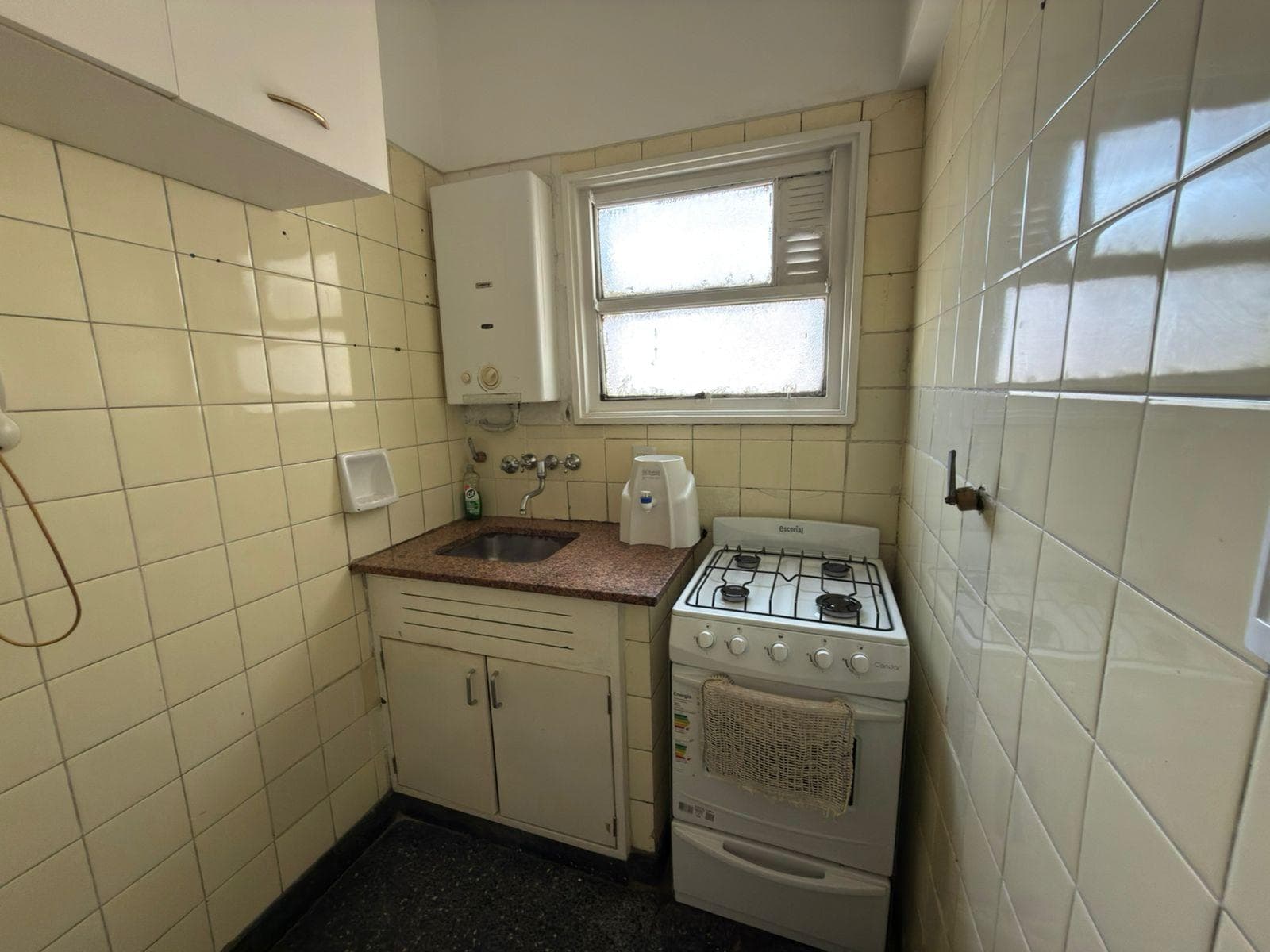 Cocina con mesada, anafe y termotanque, paredes de azulejos claros.