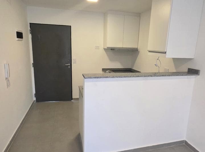 Cocina integrada con mesada, alacenas y vista a la puerta de entrada.