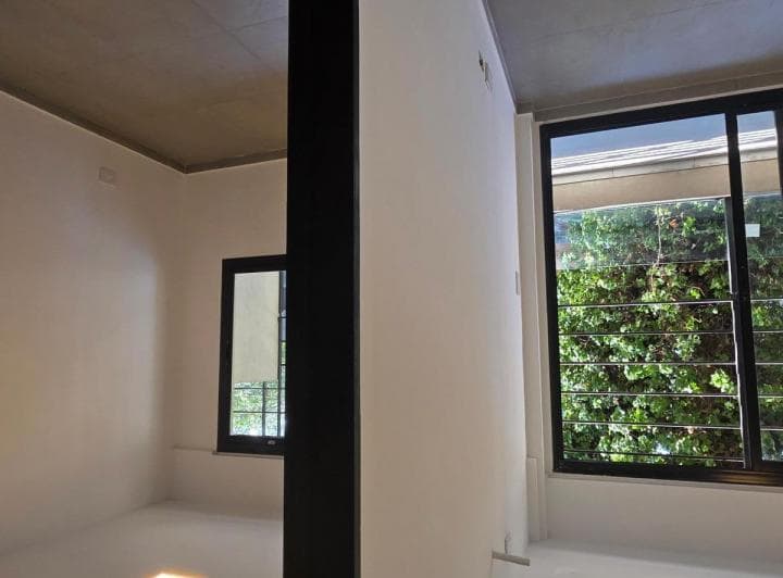 Dormitorio vacío con dos ventanas grandes con rejas y paredes blancas.