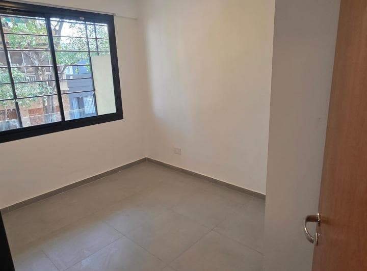 Dormitorio vacío con ventana grande con rejas y puerta de acceso.