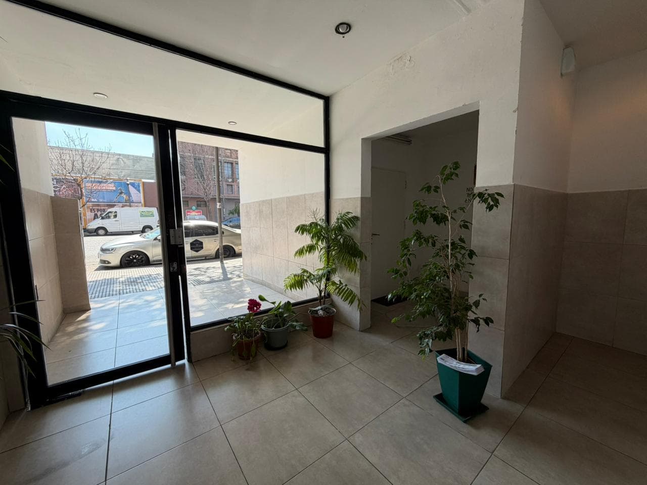 Hall de entrada del edificio con plantas y vista a la calle.