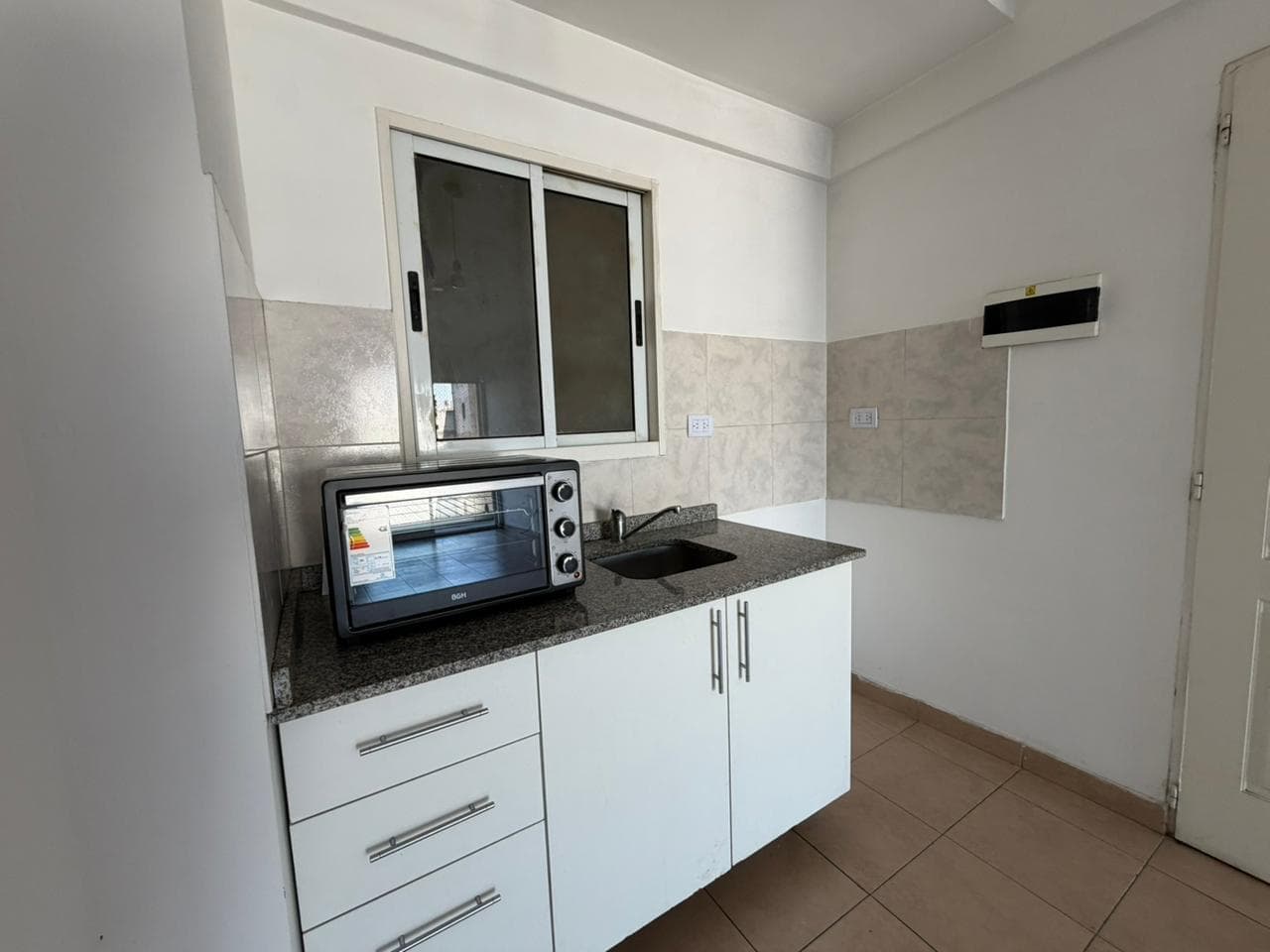 Cocina con mesada, bacha, horno microondas y ventana.