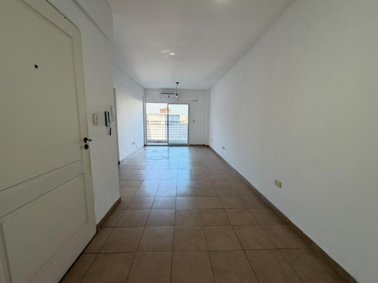 Living vacío con piso de baldosas y puerta de entrada.