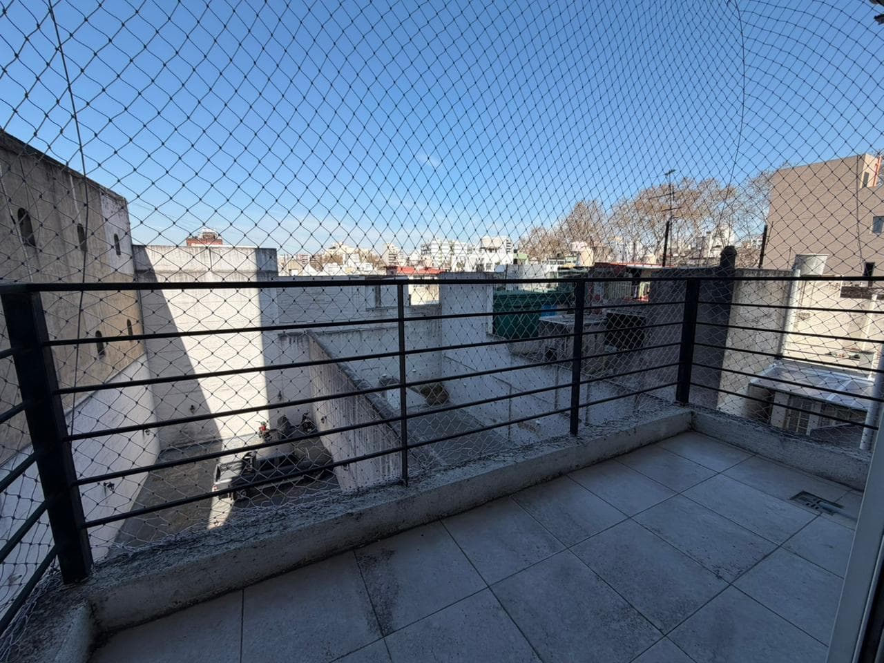 Balcón con reja y red de seguridad, vista a otros edificios.