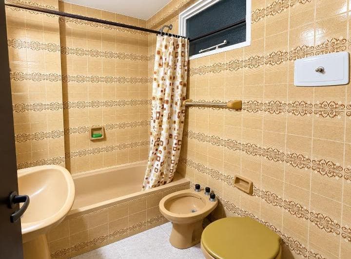 Baño con bañera, bidet, inodoro y lavatorio, con azulejos estampados amarillos.