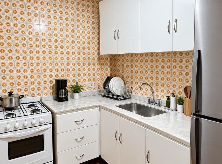 Cocina con anafe, bacha, heladera y alacenas blancas, con azulejos estampados.