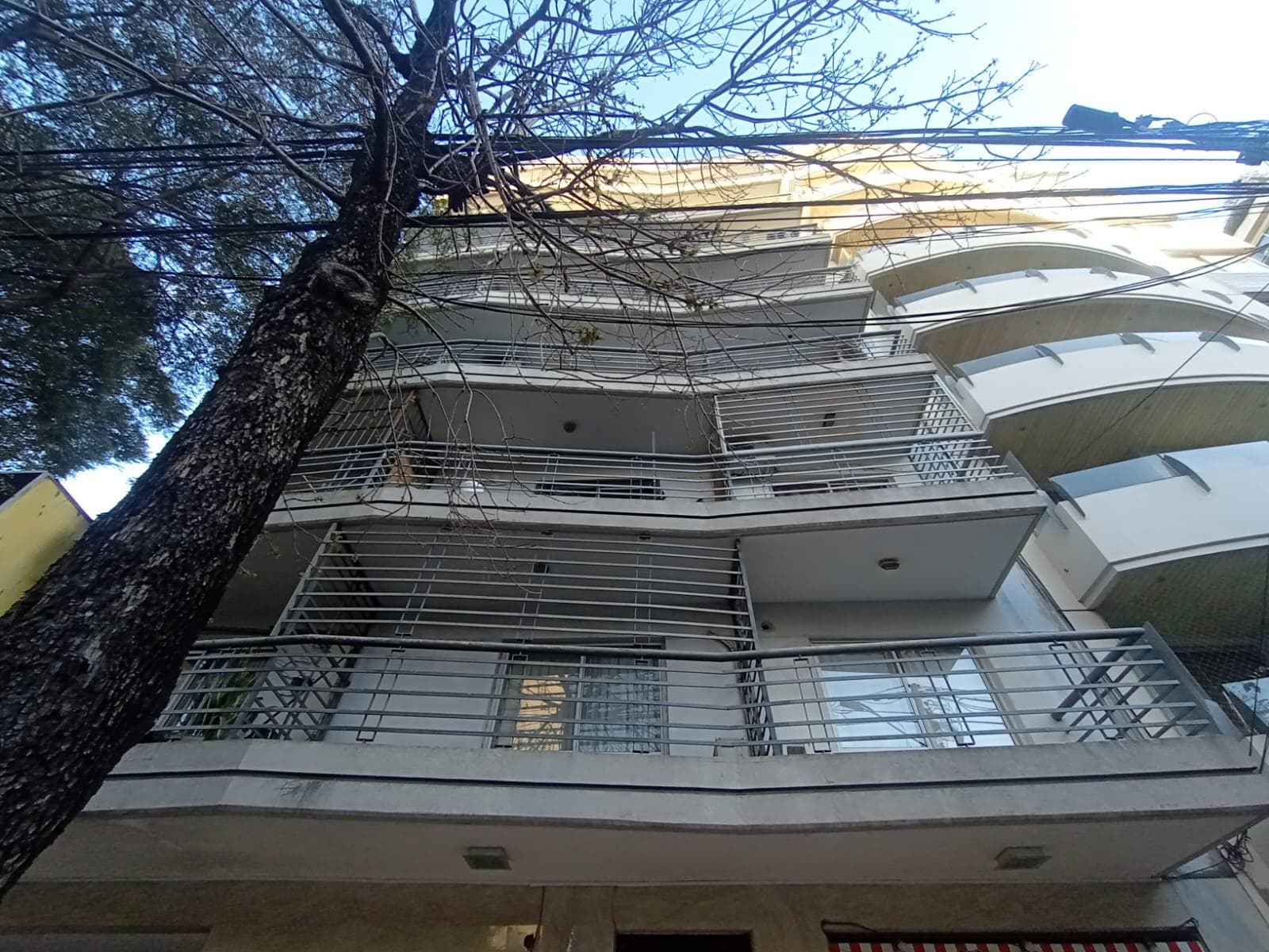 Fachada de un edificio de departamentos con balcones y árboles.