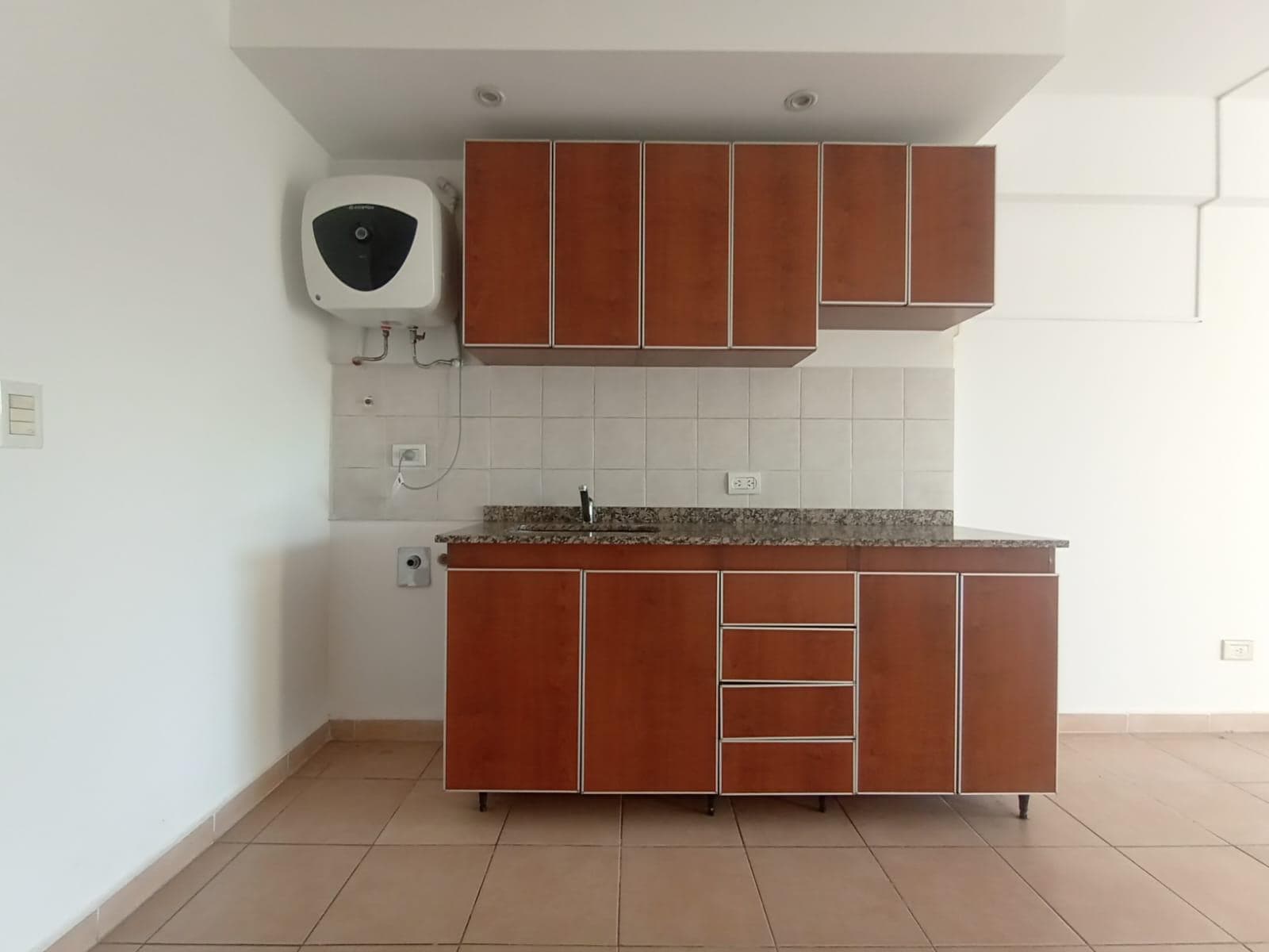Cocina integrada con mesada de granito, bacha y termotanque eléctrico.
