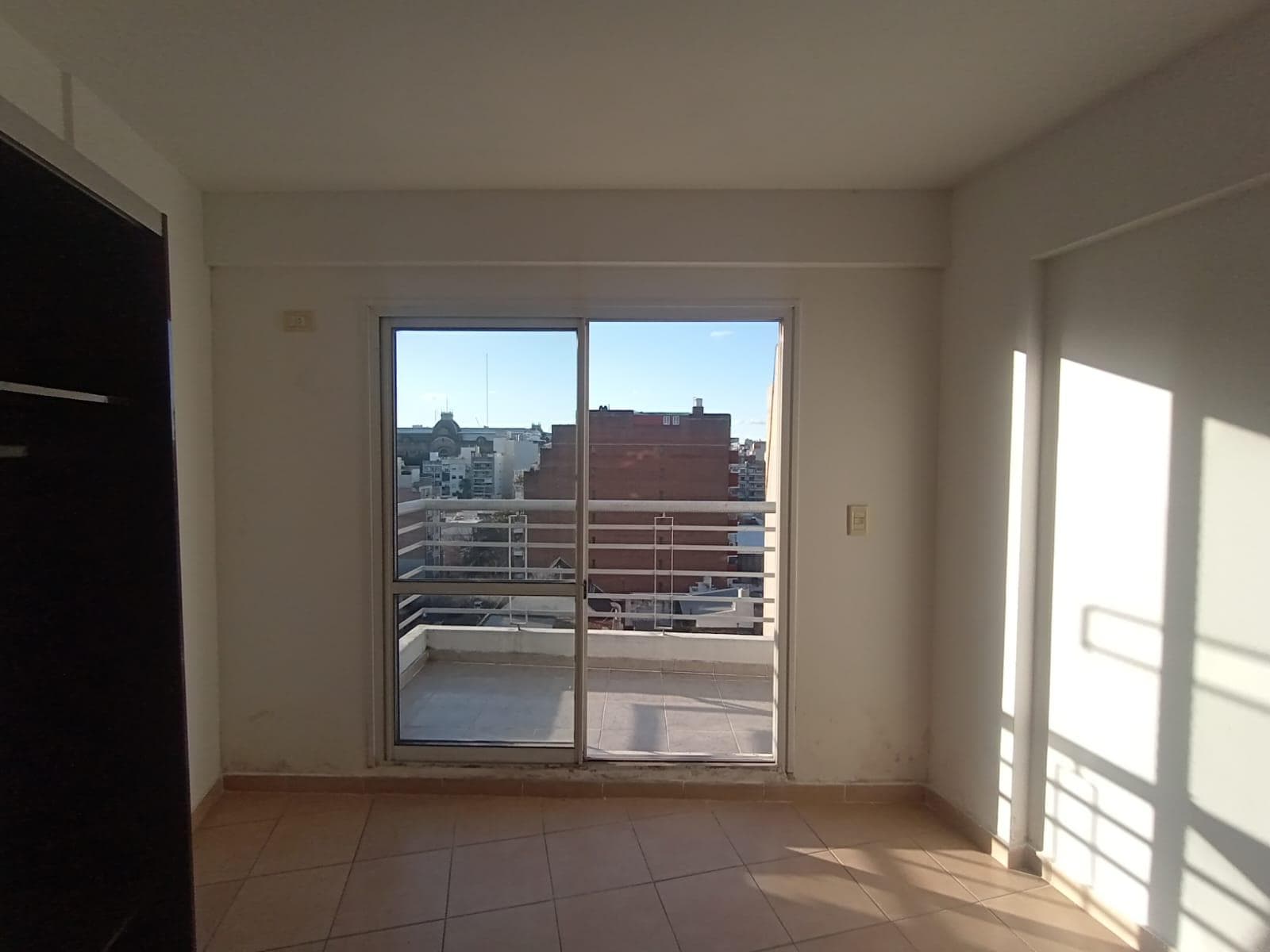 Dormitorio vacío con salida a un balcón terraza y armario oscuro.