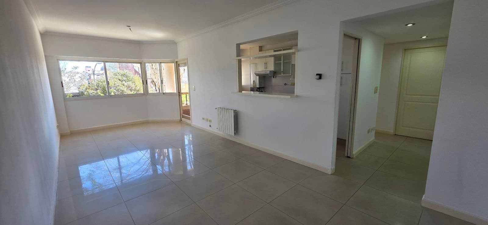 Living vacío con piso de baldosas claras y una barra pasaplatos a la cocina.