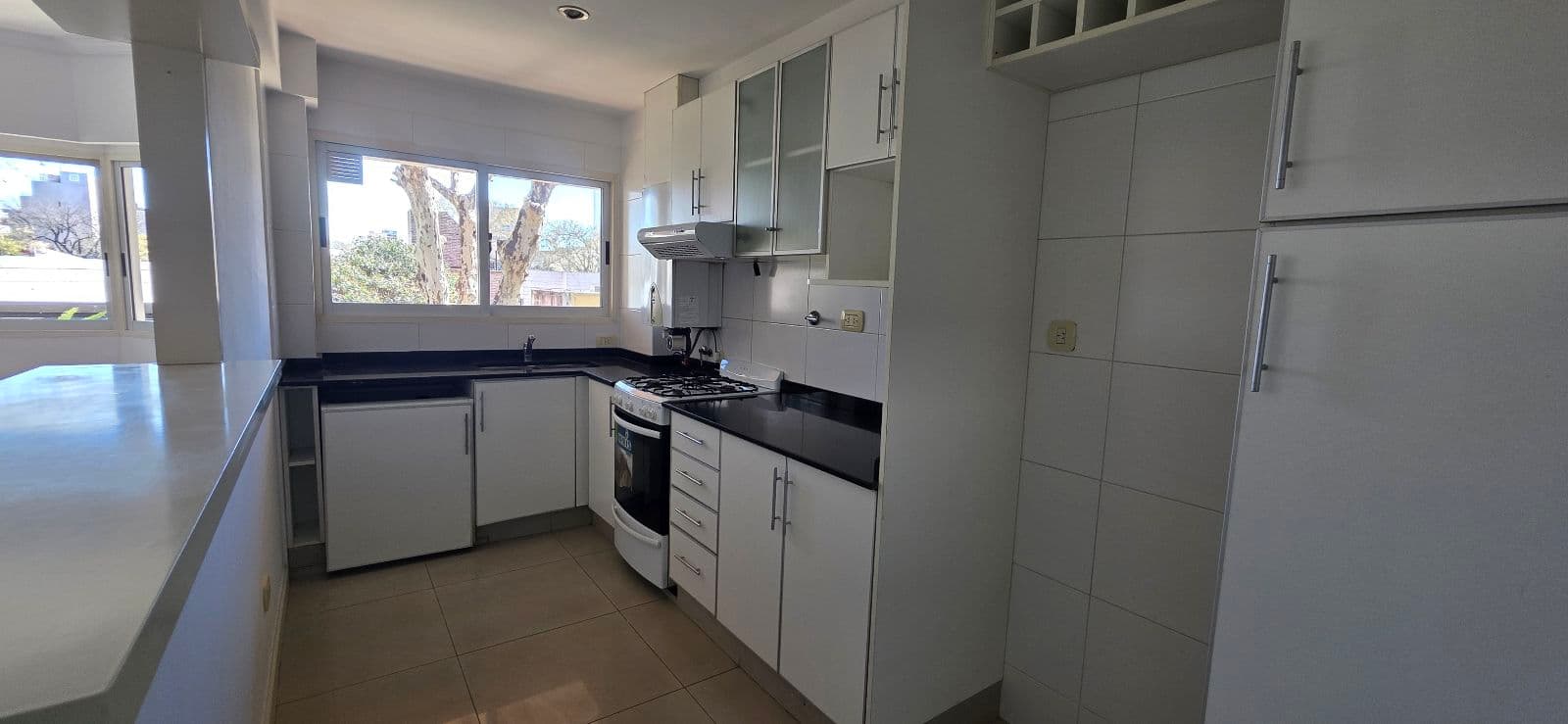 Cocina completa con muebles blancos, bacha, anafe, horno y heladera.