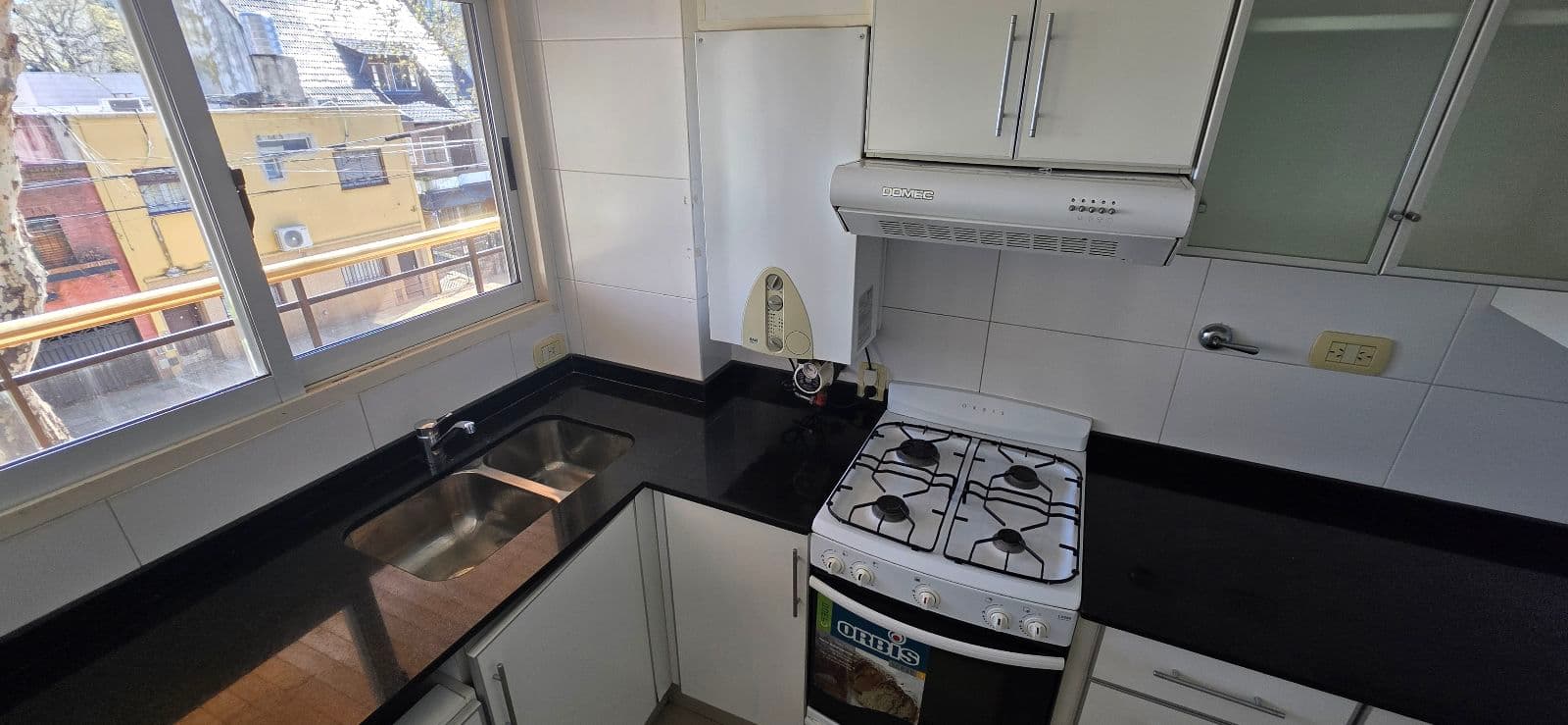 Cocina con mesada negra, bacha doble, anafe y ventana con vista.