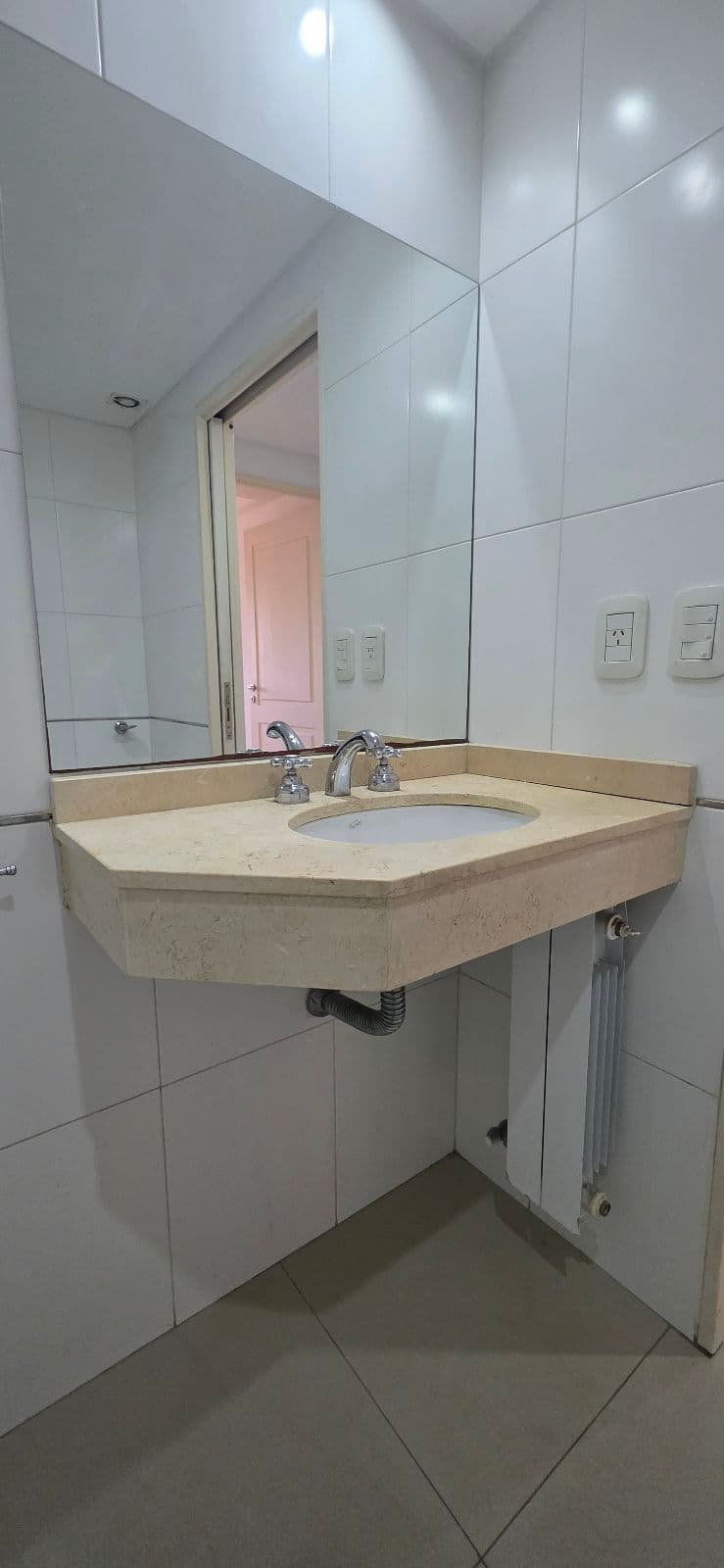 Baño con vanitory de mármol, bacha y grifería, con un gran espejo.