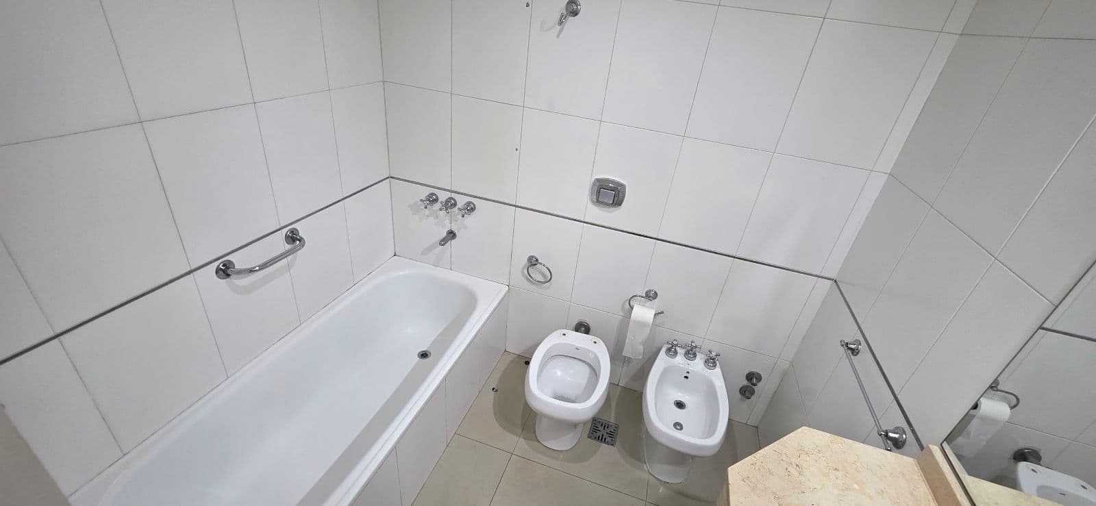 Baño completo con bañera, inodoro, bidet y azulejos blancos.